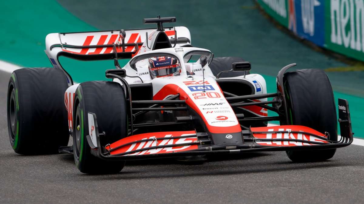 Kevin Magnussen in the cockpit during a wet Grand Prix, focused on steering and instrument panel with rain-splashed visor
