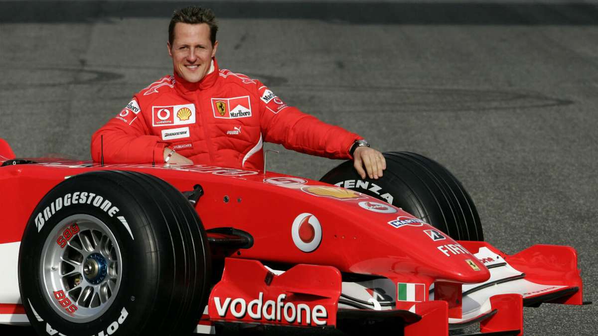 Portrait of Michael Schumacher smiling beside a vintage Formula 1 helmet
